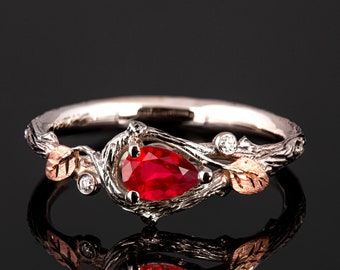 May include: A pear-shaped ruby gemstone set in a silver ring with a twig-like band and small leaves. The ring is accented with small diamonds and a gold leaf.