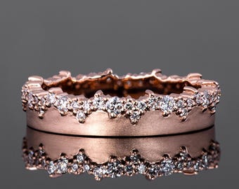 Puede incluir: Un anillo de banda de oro rosa con un borde festoneado delicado y una fila de pequeños diamantes.