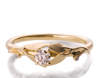May include: A gold ring with a delicate leaf design and a single round diamond in the center. The ring has two smaller diamonds on either side of the center stone.