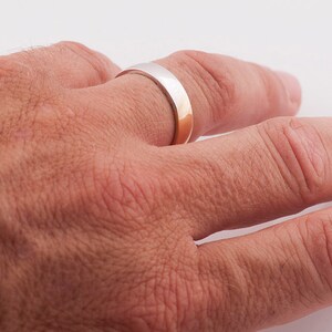 May include: A silver and gold wedding band on a person's finger.