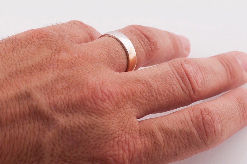 May include: A silver and gold wedding band on a person's finger.