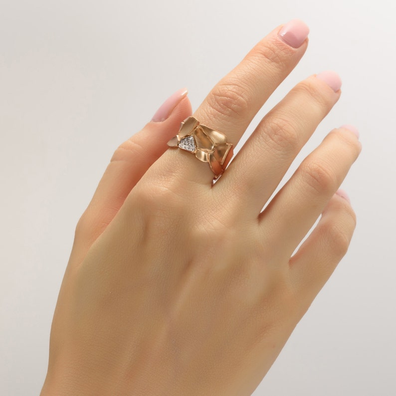 May include: A gold ring with a unique, abstract design featuring multiple overlapping pieces. The ring is set with a small, clear diamond.
