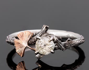 Puede incluir: Un anillo de plata y oro rosa con un diamante en bruto engastado en un diseño de rama. Una hoja de ginkgo está unida a la rama.