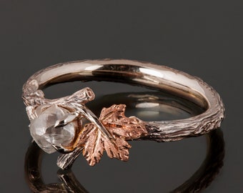 May include: A rose gold ring with a rough cut diamond set in a branch design with a leaf on the side.