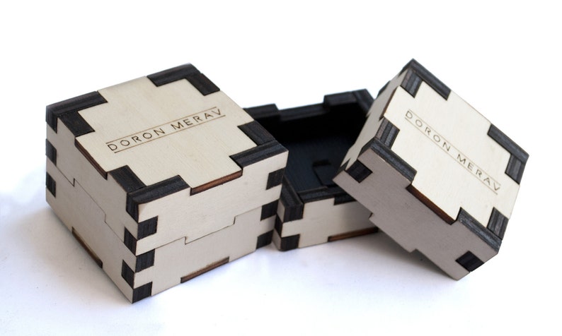May include: Three wooden boxes with black trim and the text "DORON MERAV" engraved on the top. The boxes are stacked on top of each other.