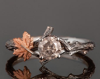 May include: A silver ring with a brown diamond set in a branch-like design. A rose gold maple leaf is attached to the branch.