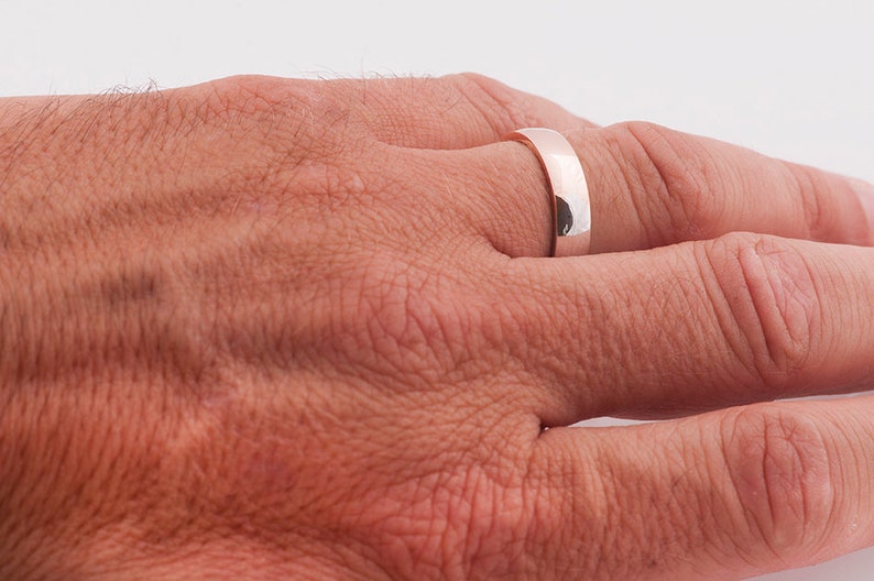 May include: A simple silver wedding band on a person's finger.