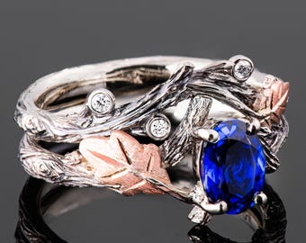 Puede incluir: Un anillo de plata y oro rosa con una piedra preciosa de zafiro azul y detalles de diamantes. El anillo presenta un diseño de rama con hojas.
