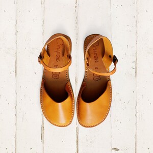 May include: A pair of tan leather sandals with ankle straps. The sandals have the word "Crypon" written on the straps and the size "38" is printed on the inside of each sandal.