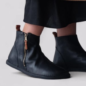 May include: Black leather ankle boots with a zipper up the front and a brown leather pull tab. The boots have a flat sole.