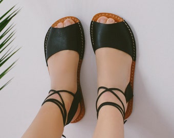 May include: Black leather sandals with brown straps and laces that tie up the legs. The sandals have an open toe design.