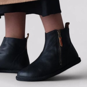 Pu&ograve; includere: Un paio di stivali da donna in pelle nera con una cerniera laterale. Gli stivali hanno una suola piatta e una punta arrotondata.