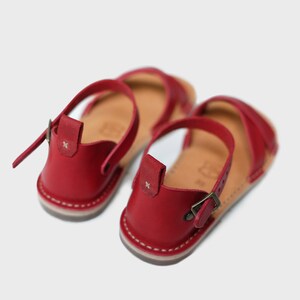 May include: A pair of red leather sandals with adjustable buckle closures. The sandals have a simple design and are perfect for summer.