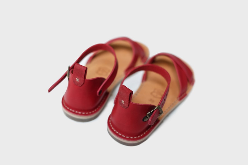 May include: A pair of red leather sandals with adjustable buckle closures. The sandals have a simple design and are perfect for summer.