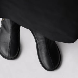Pu&ograve; includere: Un paio di stivaletti in pelle nera con punta a punta e cerniera laterale.