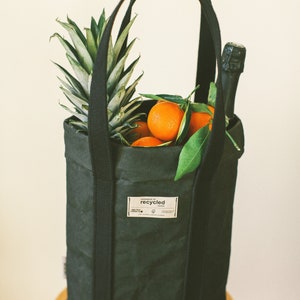 May include: A black tote bag made of recycled paper, filled with oranges and a pineapple. The bag has a label that says "Handmade of recycled paper".