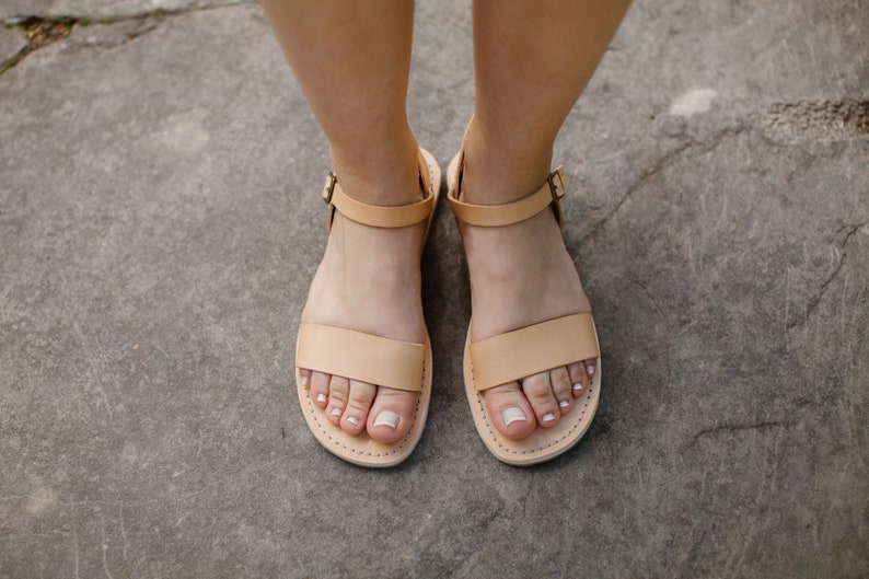 May include: A pair of light brown leather sandals with ankle straps. The sandals have a simple design and are perfect for summer.