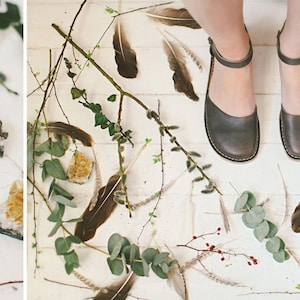 May include: A pair of brown leather ankle strap sandals with a white background featuring antlers, feathers, and greenery.