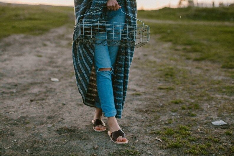 May include: A person wearing blue jeans and a striped blanket walks down a dirt path while carrying a wire basket.