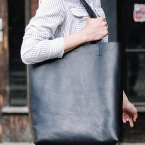 May include: A black leather tote bag with a long strap. The bag is large enough to carry a laptop or other items.