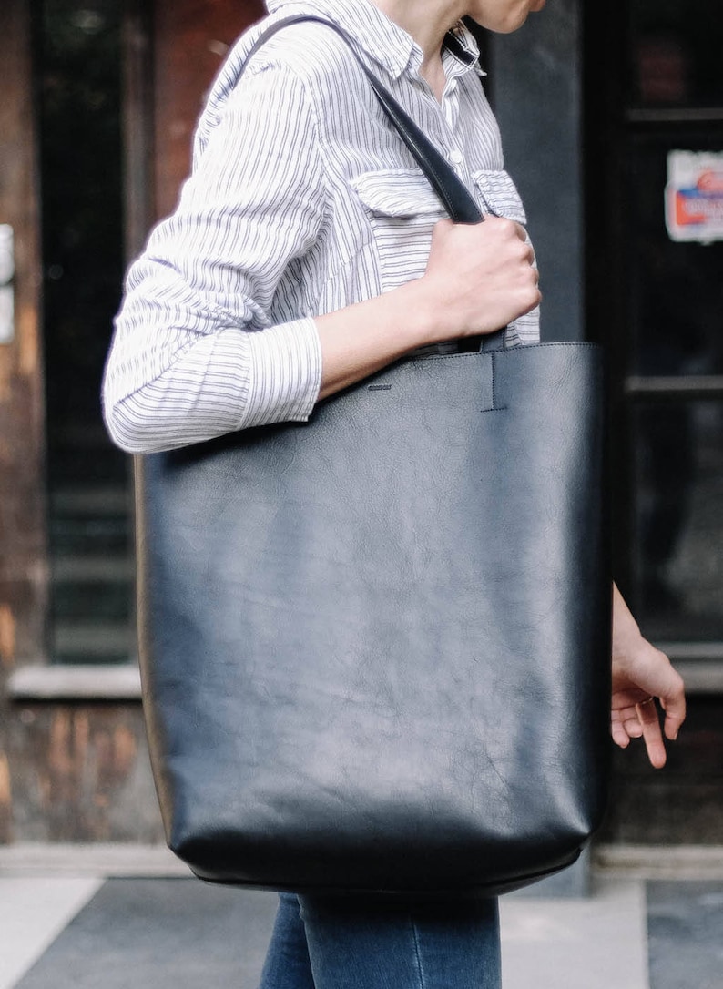 May include: A black leather tote bag with a long strap. The bag is large enough to carry a laptop or other items.