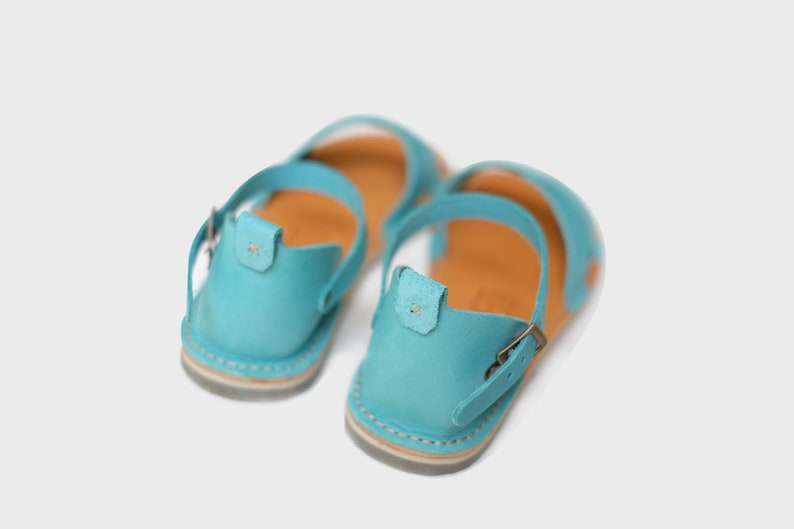 May include: A pair of light blue leather sandals with a buckle closure. The sandals have a brown leather insole and a white sole.