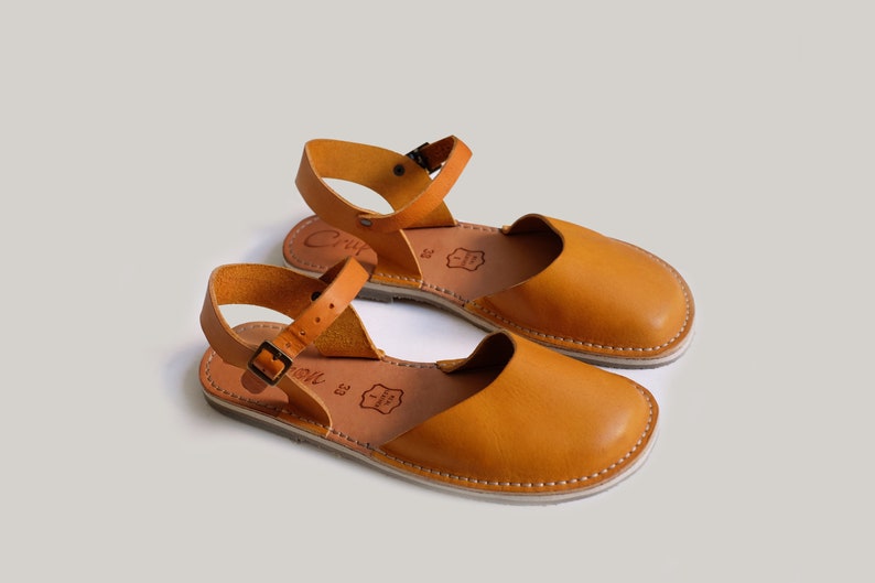 May include: A pair of tan leather sandals with ankle straps and buckles. The sandals have a simple design and are made of high-quality leather.
