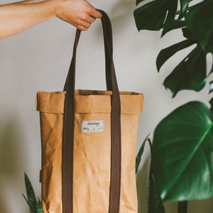 May include: A brown paper tote bag with brown straps. The bag has a white label that says "recycled" on it.