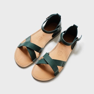 May include: A pair of dark green leather sandals with criss-cross straps and an ankle strap.