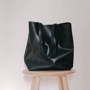 May include: A black leather tote bag with two handles, sitting on a wooden stool.