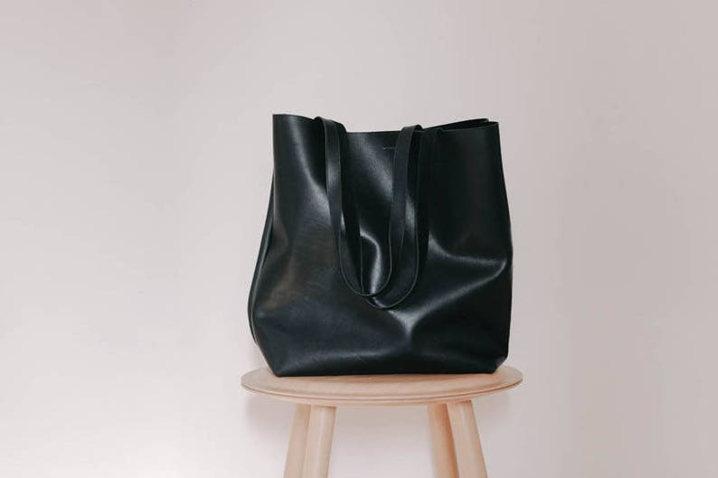 May include: A black leather tote bag with two handles, sitting on a wooden stool.