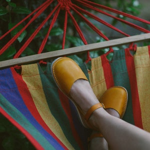 May include: A person relaxing in a colorful striped hammock with their feet in yellow leather sandals.
