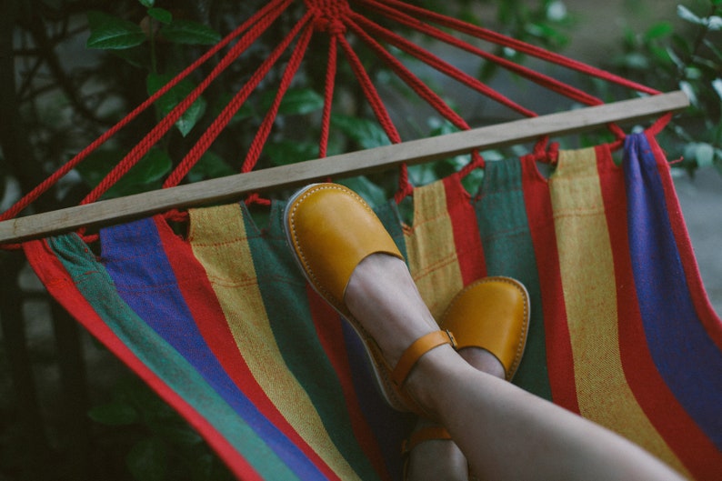 May include: A person relaxing in a colorful striped hammock with their feet in yellow leather sandals.