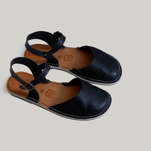 Pode incluir: Um par de sand&aacute;lias de couro preto com uma tira no tornozelo e uma sola branca. As sand&aacute;lias t&ecirc;m um design simples e s&atilde;o perfeitas para o ver&atilde;o.