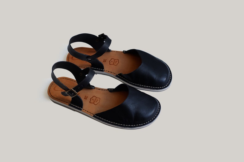 Pode incluir: Um par de sand&aacute;lias de couro preto com uma tira no tornozelo e uma sola branca. As sand&aacute;lias t&ecirc;m um design simples e s&atilde;o perfeitas para o ver&atilde;o.