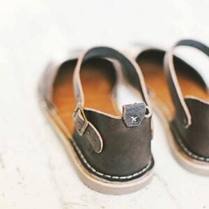 May include: A pair of brown leather sandals with adjustable straps and a buckle closure. The sandals have a simple design and are made of high-quality leather.