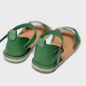 May include: A pair of green leather sandals with adjustable ankle straps and buckles. The sandals have a brown leather insole and a light brown sole.