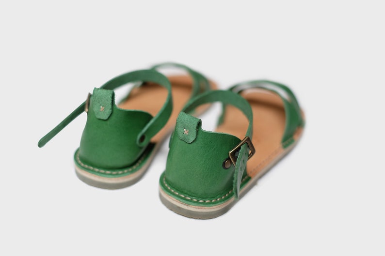 May include: A pair of green leather sandals with adjustable ankle straps and buckles. The sandals have a brown leather insole and a light brown sole.