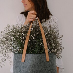 May include: A gray felt tote bag with brown leather handles. The bag is filled with a bouquet of white baby's breath flowers.