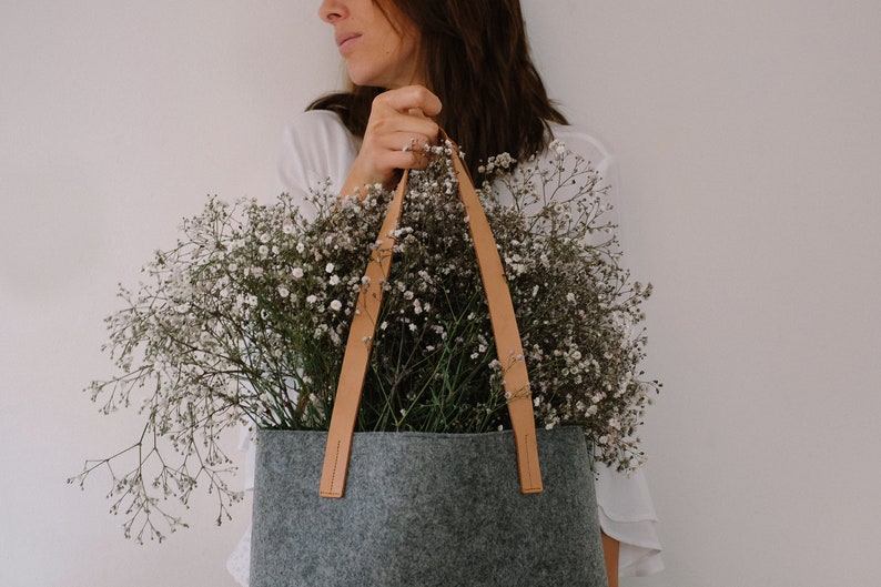 May include: A gray felt tote bag with brown leather handles. The bag is filled with a bouquet of white baby's breath flowers.