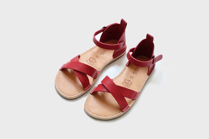 May include: A pair of red leather sandals with criss-cross straps and an ankle strap with a buckle closure.
