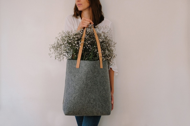 May include: A gray felt tote bag with brown leather handles, filled with a bouquet of white baby's breath flowers.