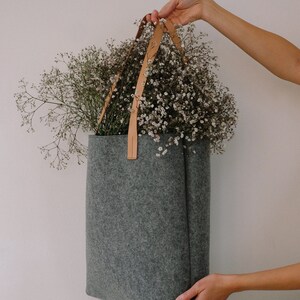 May include: A gray felt tote bag with brown leather straps, filled with a bouquet of white baby's breath flowers.