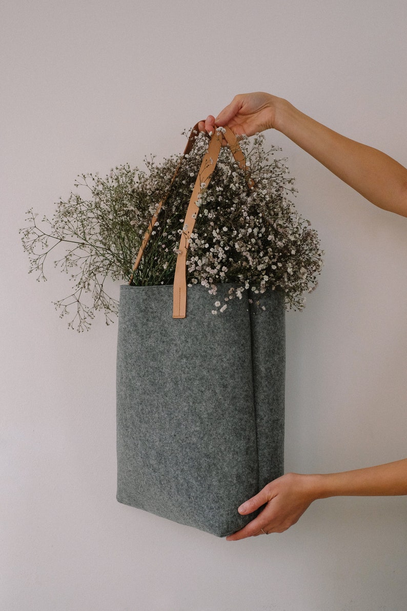 May include: A gray felt tote bag with brown leather straps, filled with a bouquet of white baby's breath flowers.