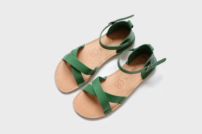 May include: A pair of green leather sandals with a buckle closure. The sandals have a criss-cross strap design and a brown leather sole.