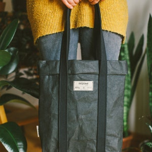 May include: A black tote bag made from recycled paper with black straps. The bag has a label that says "made of recycled paper".
