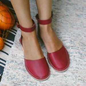 May include: A pair of burgundy leather sandals with ankle straps. The sandals have a simple design and are made of soft, supple leather.
