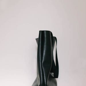May include: A black leather tote bag with a single strap. The bag is sitting on a light wood table.