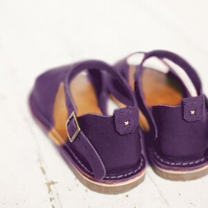May include: A pair of purple leather sandals with a buckle strap and a brown sole.