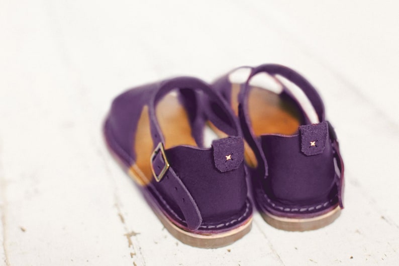 May include: A pair of purple leather sandals with a buckle strap and a brown sole.